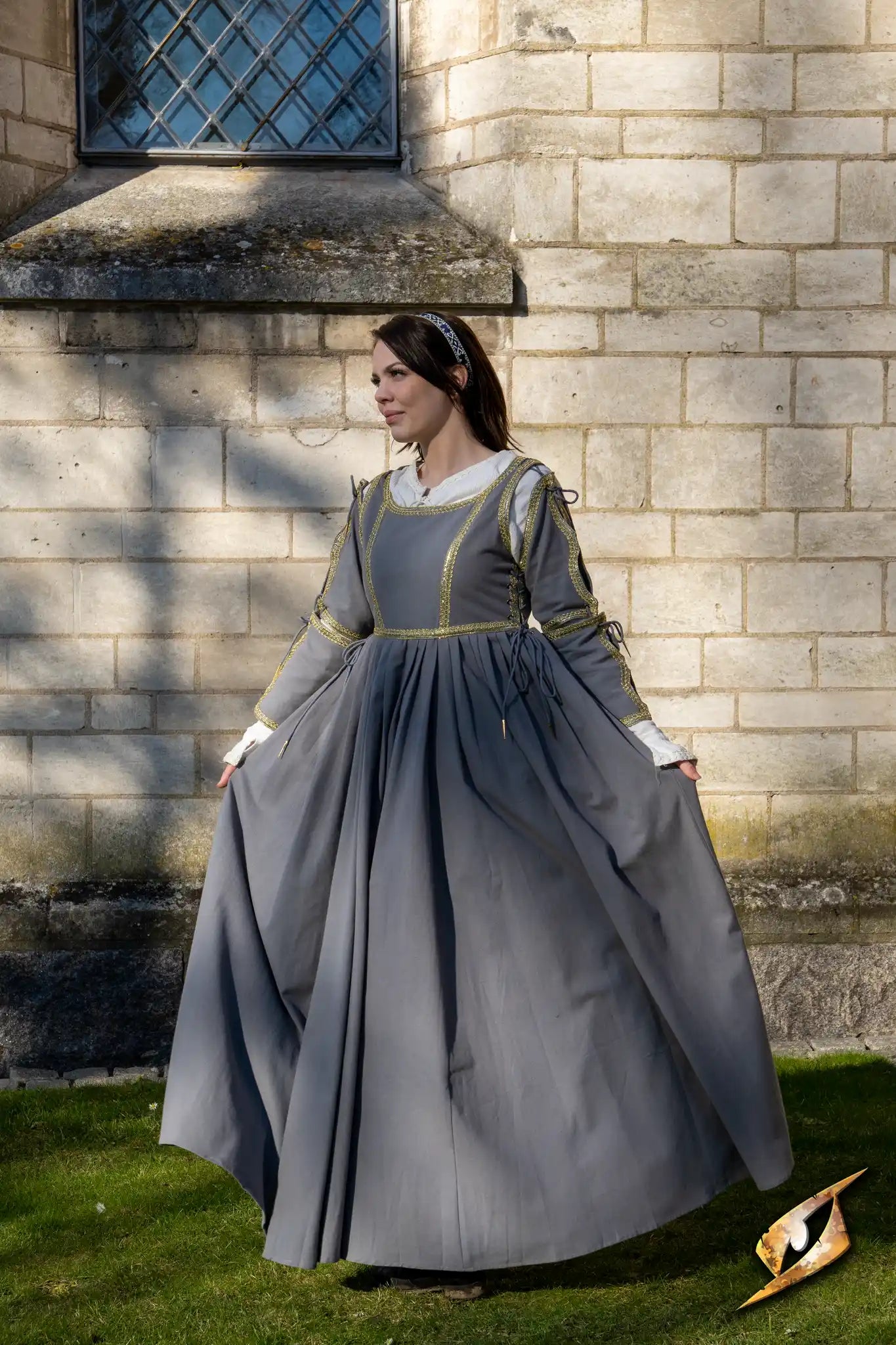 Elegant Dress Lucrezia showcased on a model outdoors, featuring golden trimmings and flowing grey fabric.