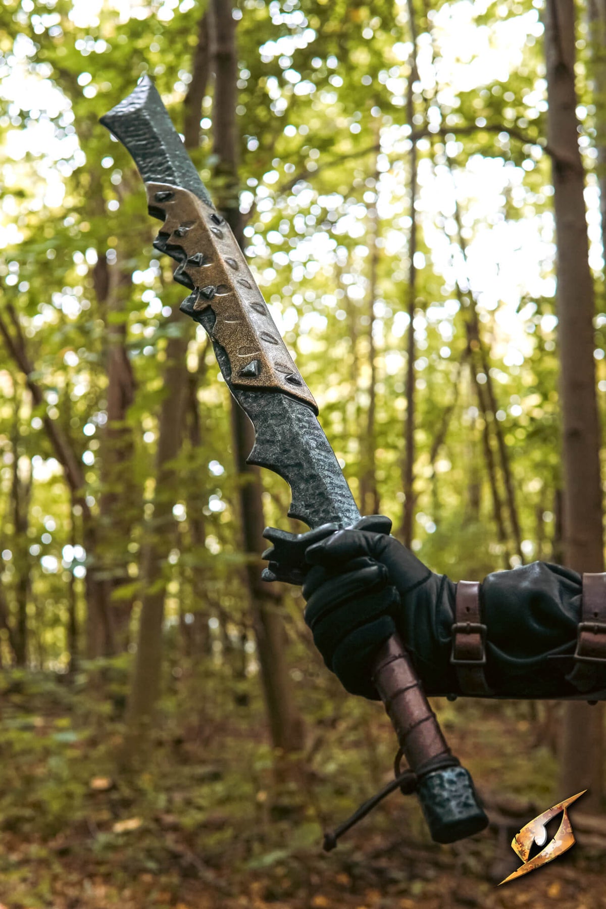 A fantasy curved sword with a textured dark gray blade and bronze-colored guard, held by a hand wearing a black glove in a forest setting.