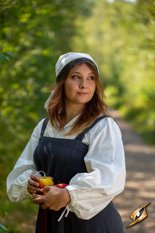 Woman in a countryside scene wearing a white headscarf and holding apples, representing the Estrid Scarf's story.