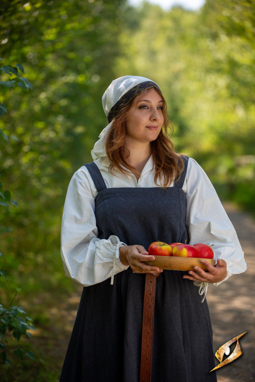 Woman in traditional attire holding apples, walking along a wooded path, symbolizing rural life.