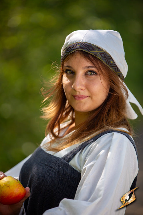 Portrait of a woman wearing a scarf and holding an apple in a green outdoor setting.