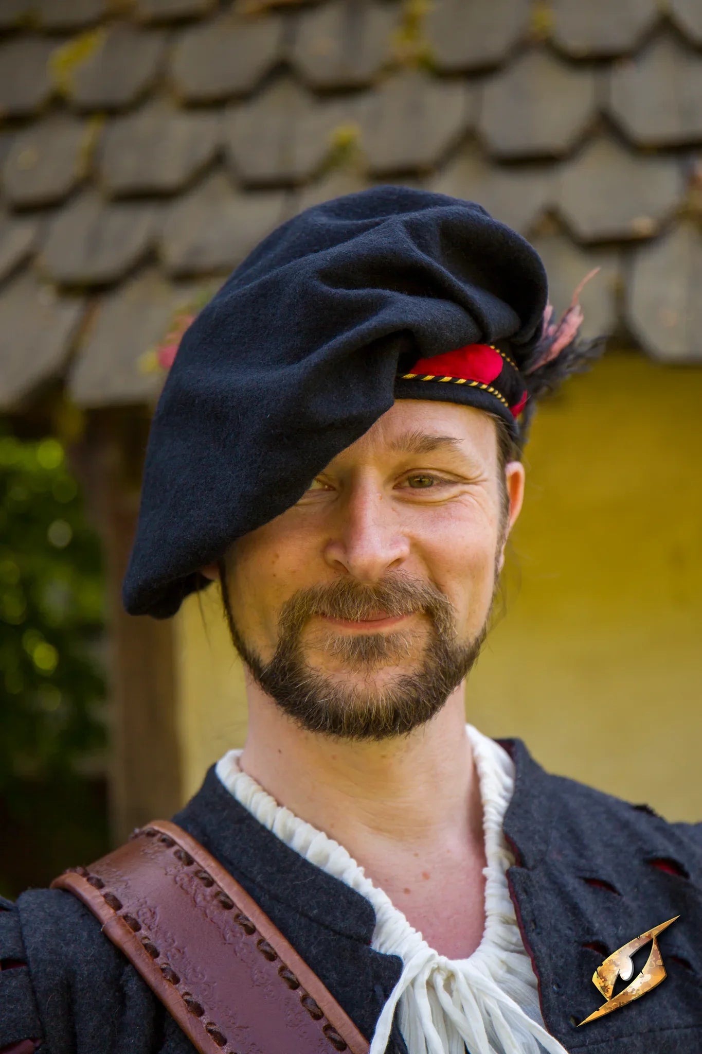 Wool Minstrel Hat worn by a smiling man in period costume, featuring a colorful feather and historic attire.