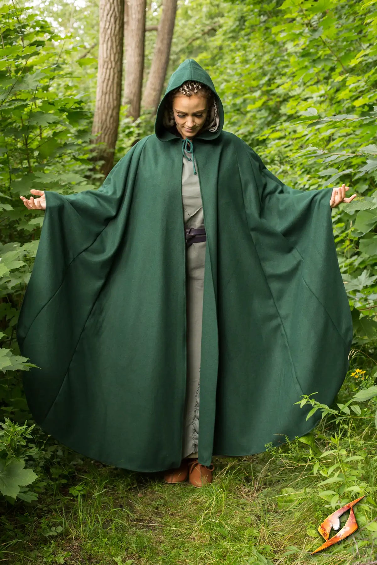 Woman wearing the Cape Godfrey Wool in a lush green forest, showcasing its hooded design and flowing silhouette.