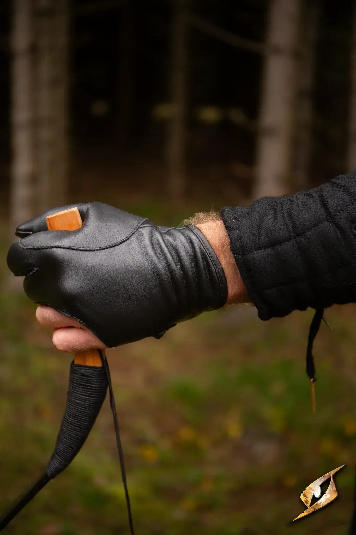 A hand wearing an Archery Half-glove, holding a bowstring in a natural setting, showcasing precision and comfort.