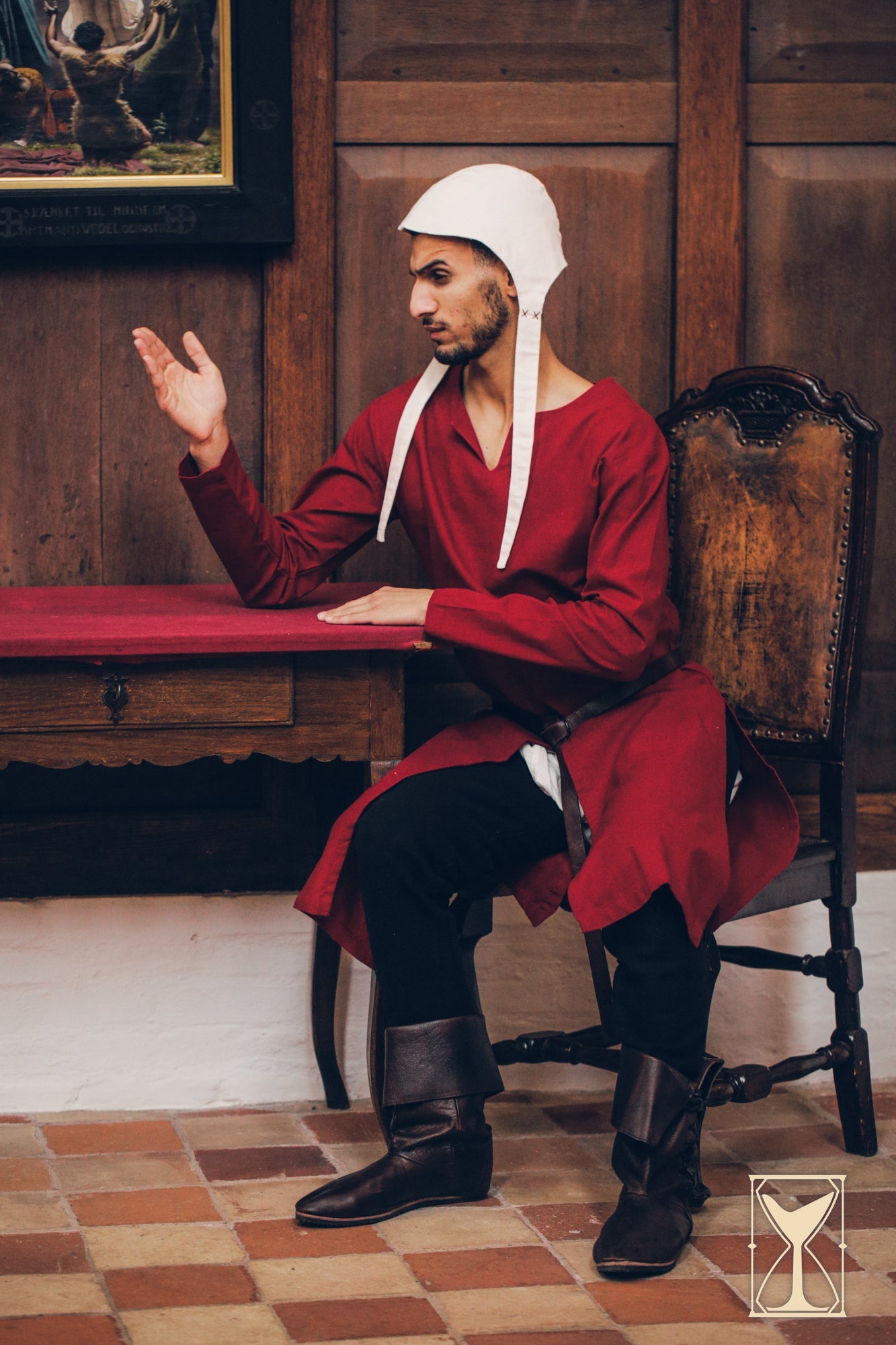 Medieval Riding Tunic worn by a model sitting at a table, showcasing its classic design and functionality.