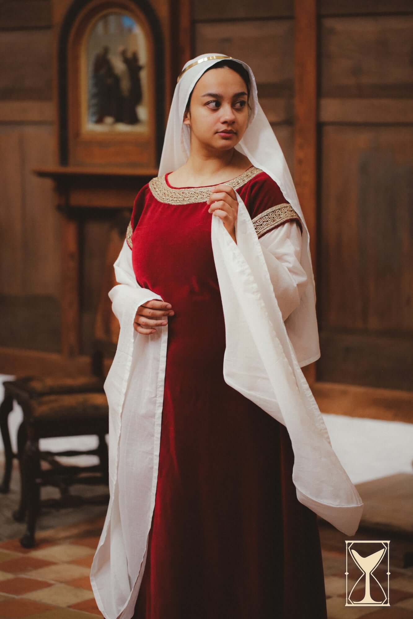 Bliaut Noble dress featuring rich velvet and flowing sleeves, modeled in an indoor medieval setting.