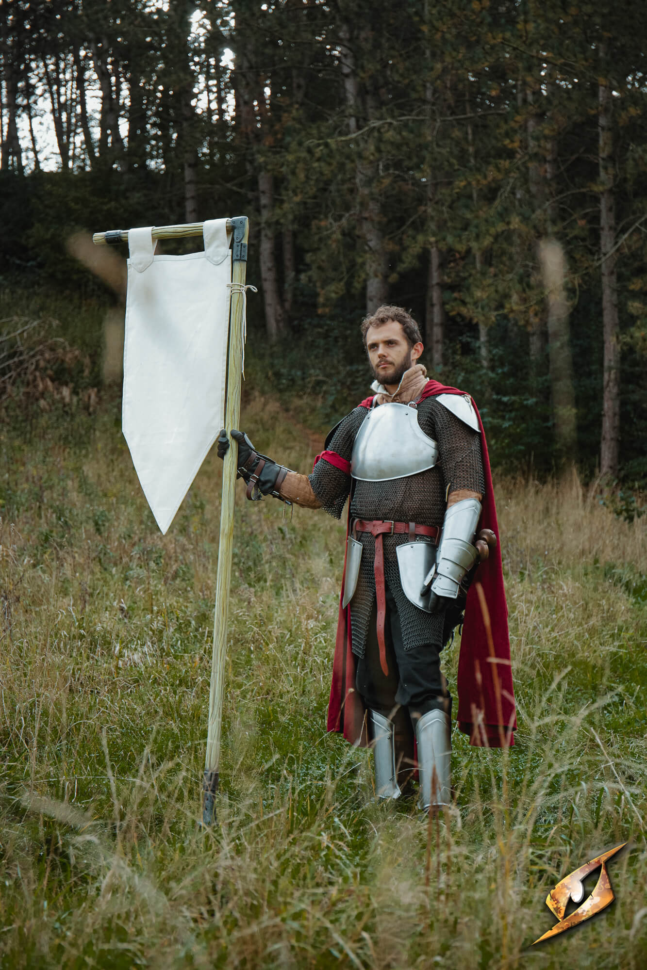 A person in armor holding a Complete Battle Standard Set - L-Top banner pole in a natural setting.