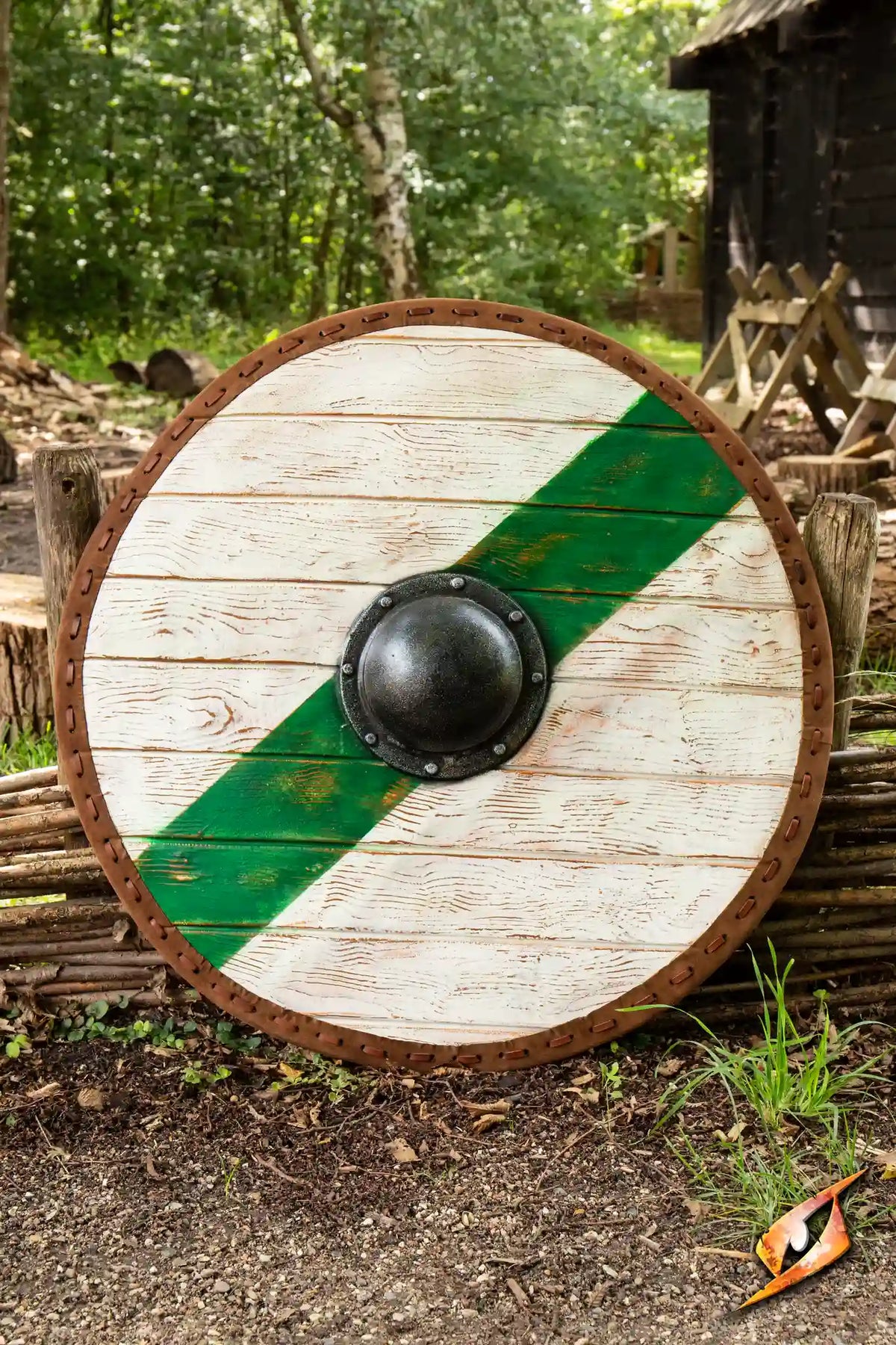Thegn Shield featuring a round design with a green diagonal stripe and central black boss in a forest setting.