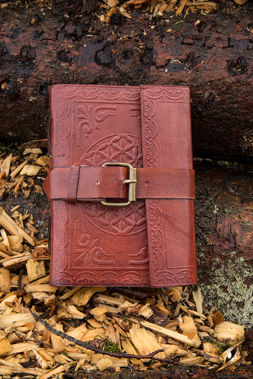 Leather Diary resting on wood shavings, showcasing its intricate design and sturdy buckle closure.