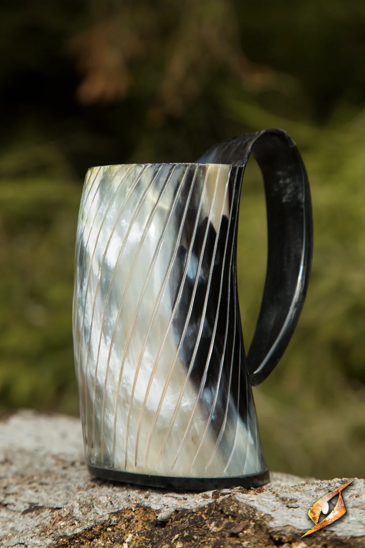 Decorative horn mug with black handle on a natural stone surface with blurred greenery in the background