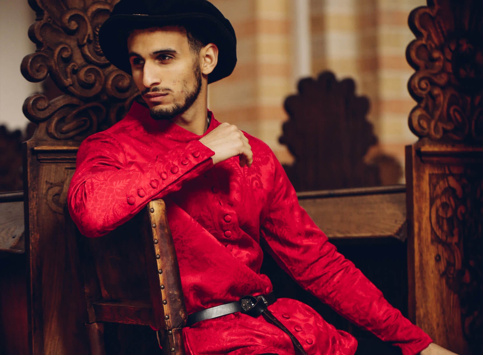 Man in red patterned tunic and black hat, representing Late Medieval fashion.