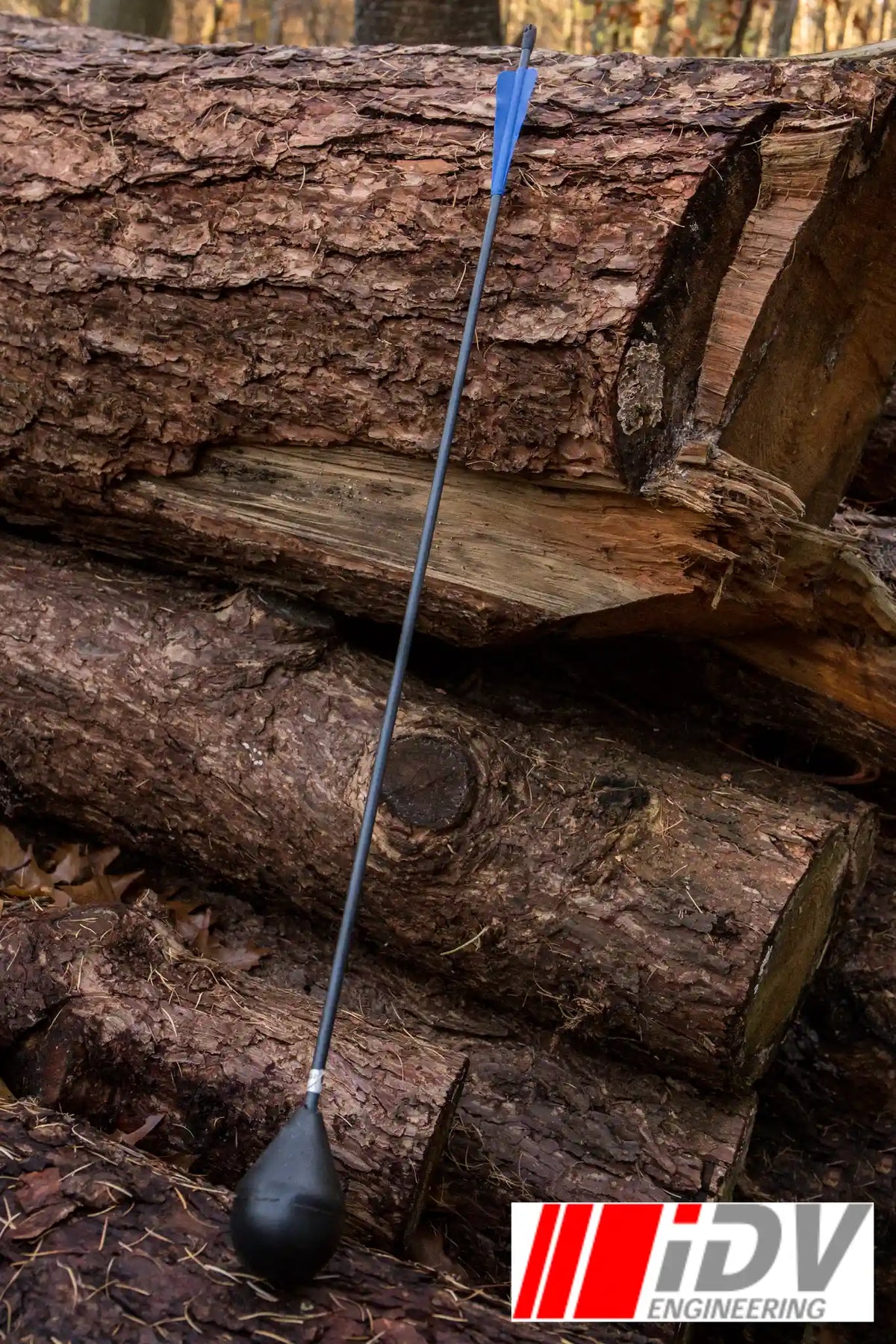 Arrow - Round Head - Black Shaft resting against logs in a forest setting, showcasing its streamlined design.