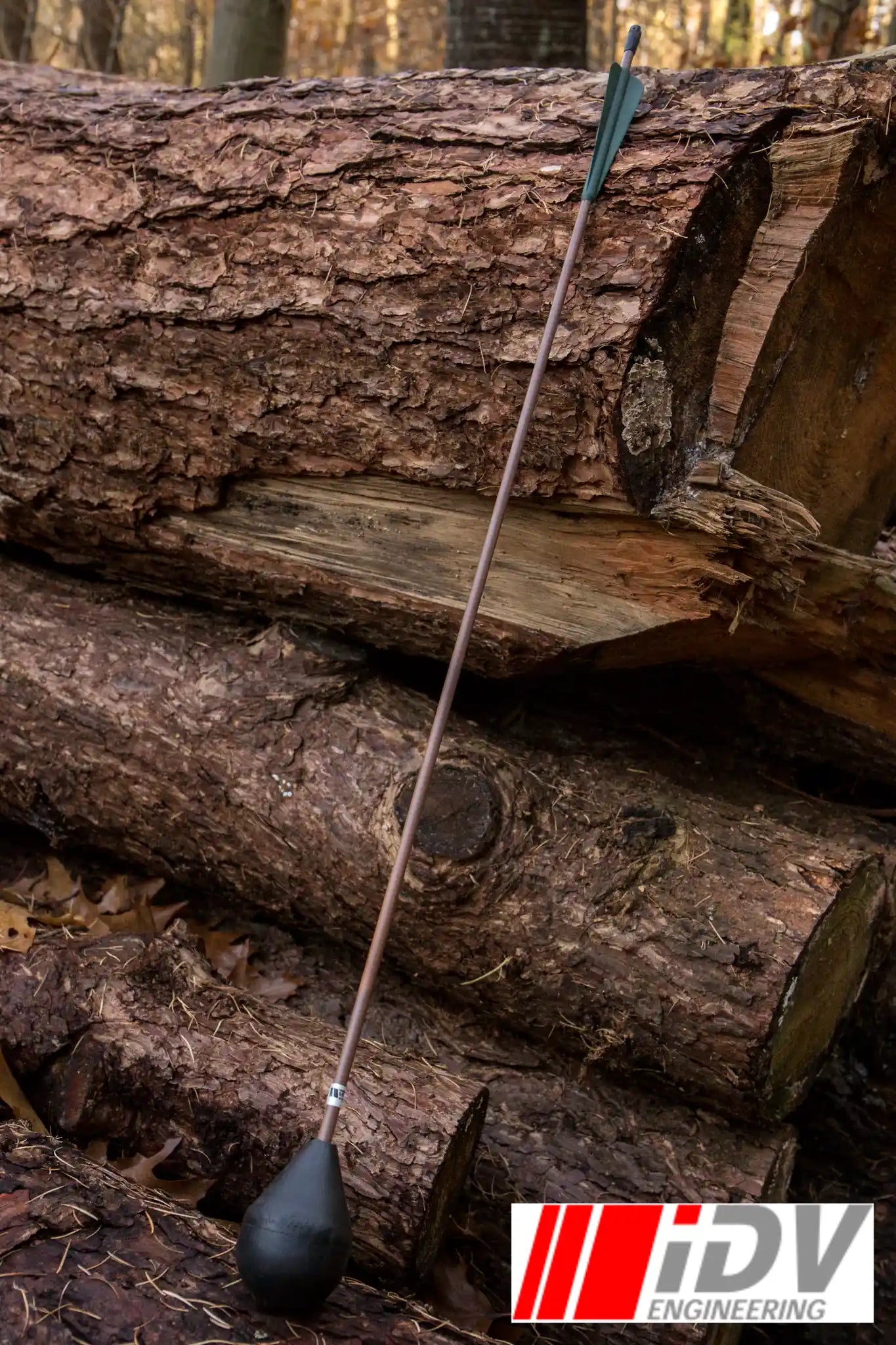 Arrow - Round Head - Brown Shaft leaning against a stack of logs in a woodland setting. Ideal for archery enthusiasts.
