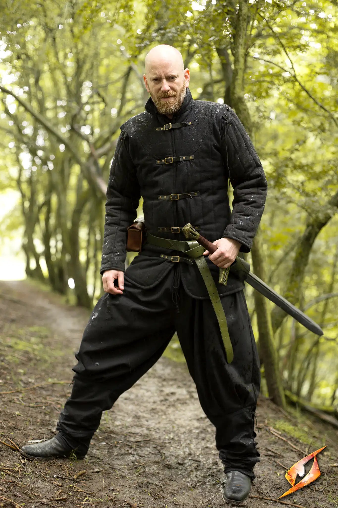 Gambeson Warrior With Long Sleeves standing confidently in a forest, holding a sword, showcasing medieval armor.