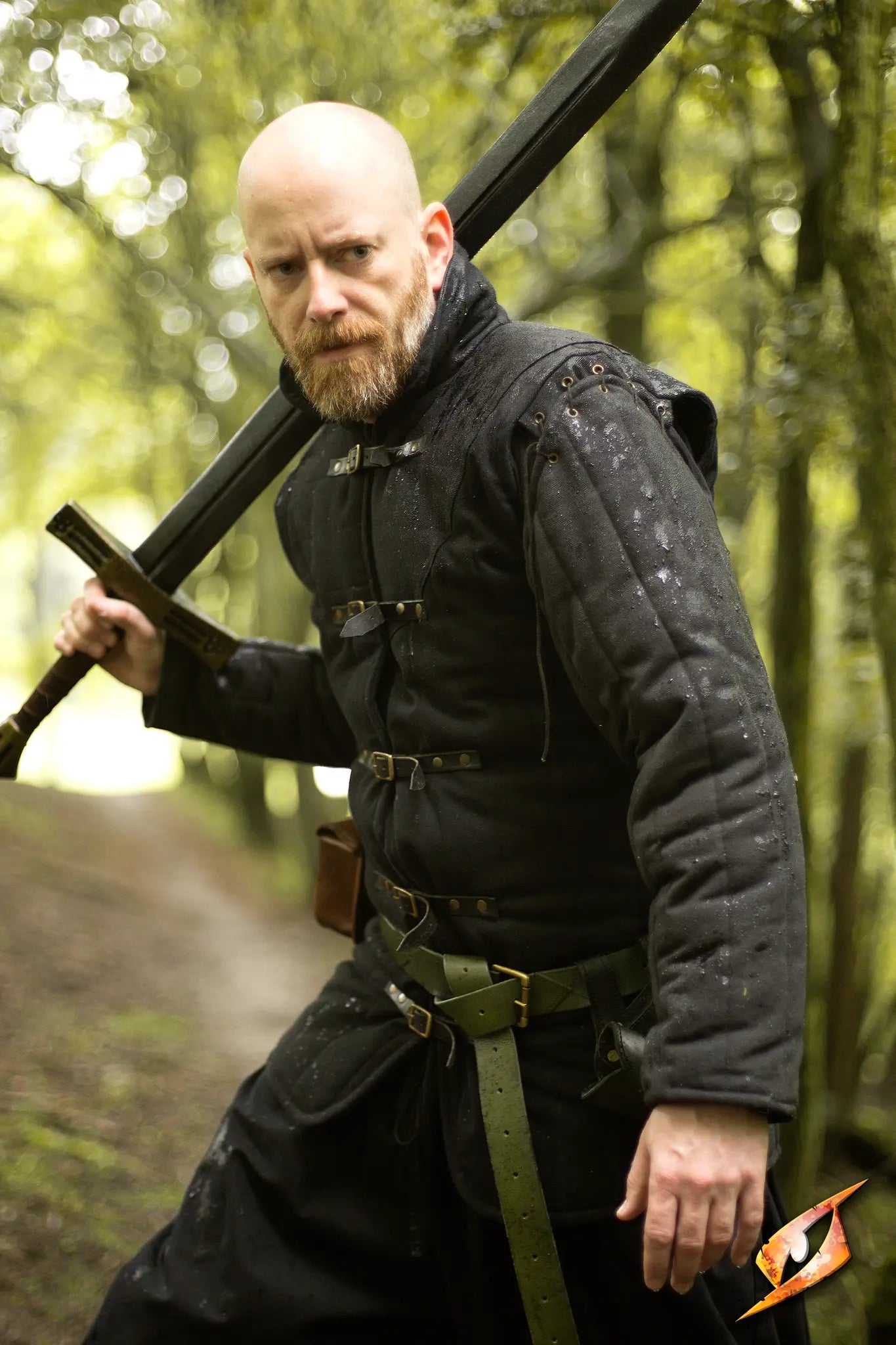 Gambeson Warrior With Long Sleeves standing fiercely in a forest, wielding a sword with a serious expression.