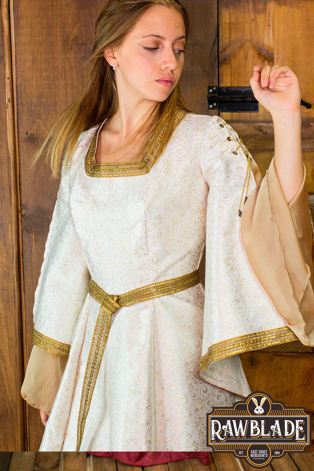 Aquitania Noble Dress worn by a model showcasing its gold trims and tulle sleeves against a wooden background.