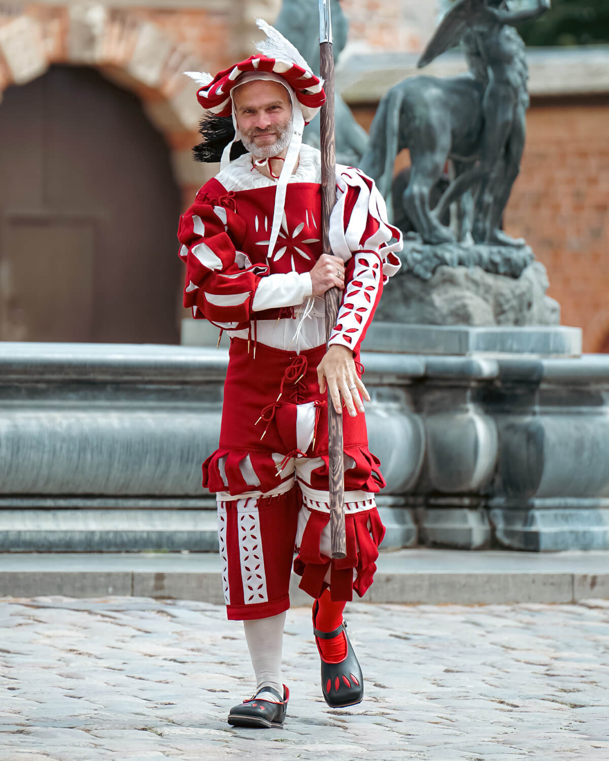 Man in red Landsknecht Garb with spear, showing historical Renaissance style outfit.