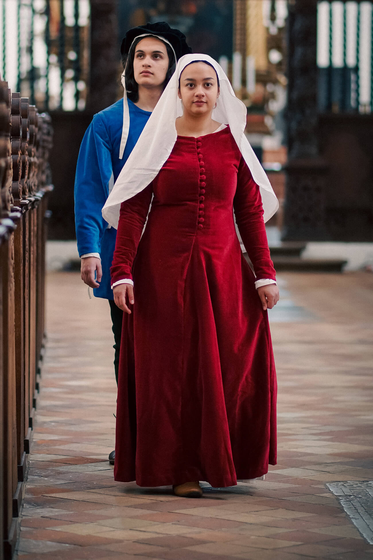 Two people in period costumes walking through a cathedral.