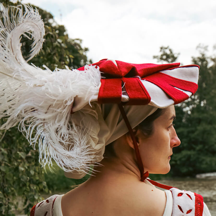 Person wearing a traditional landsknecht hat with red and white colors, outdoors.