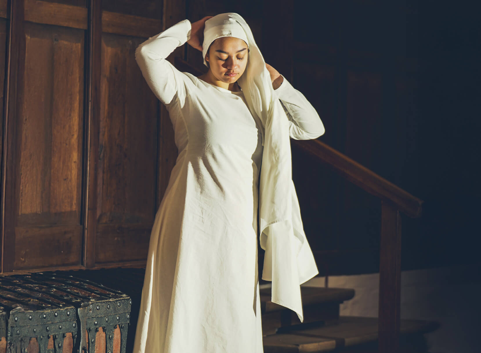 Woman in white Late Medieval dress and wimple adjusting her head covering.