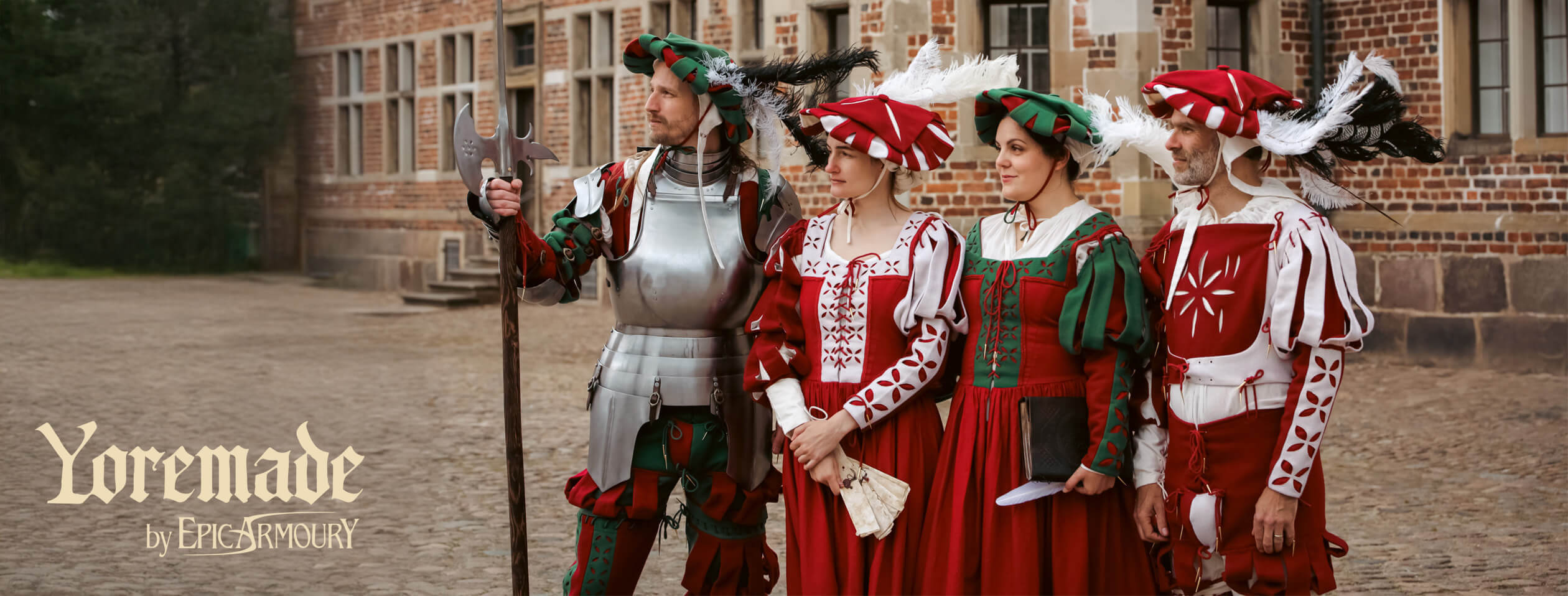 Four individuals in medieval costumes standing in front of a brick building.