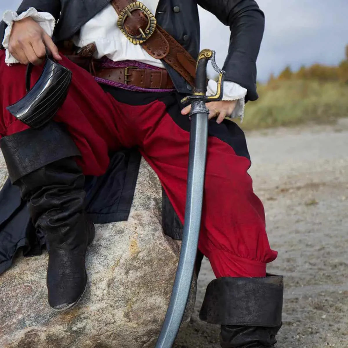 Curved Cores pirate character wearing red pants, black boots, holding a sword while sitting on a rock.