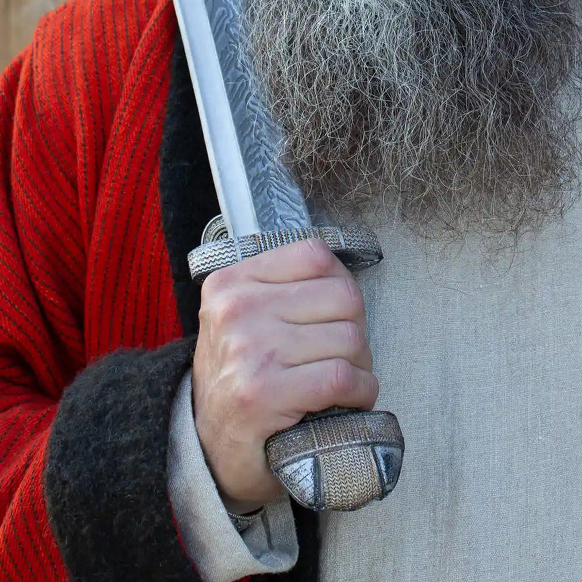 A close-up of a hand gripping The EirikR Sword with intricate detailing on the hilt.