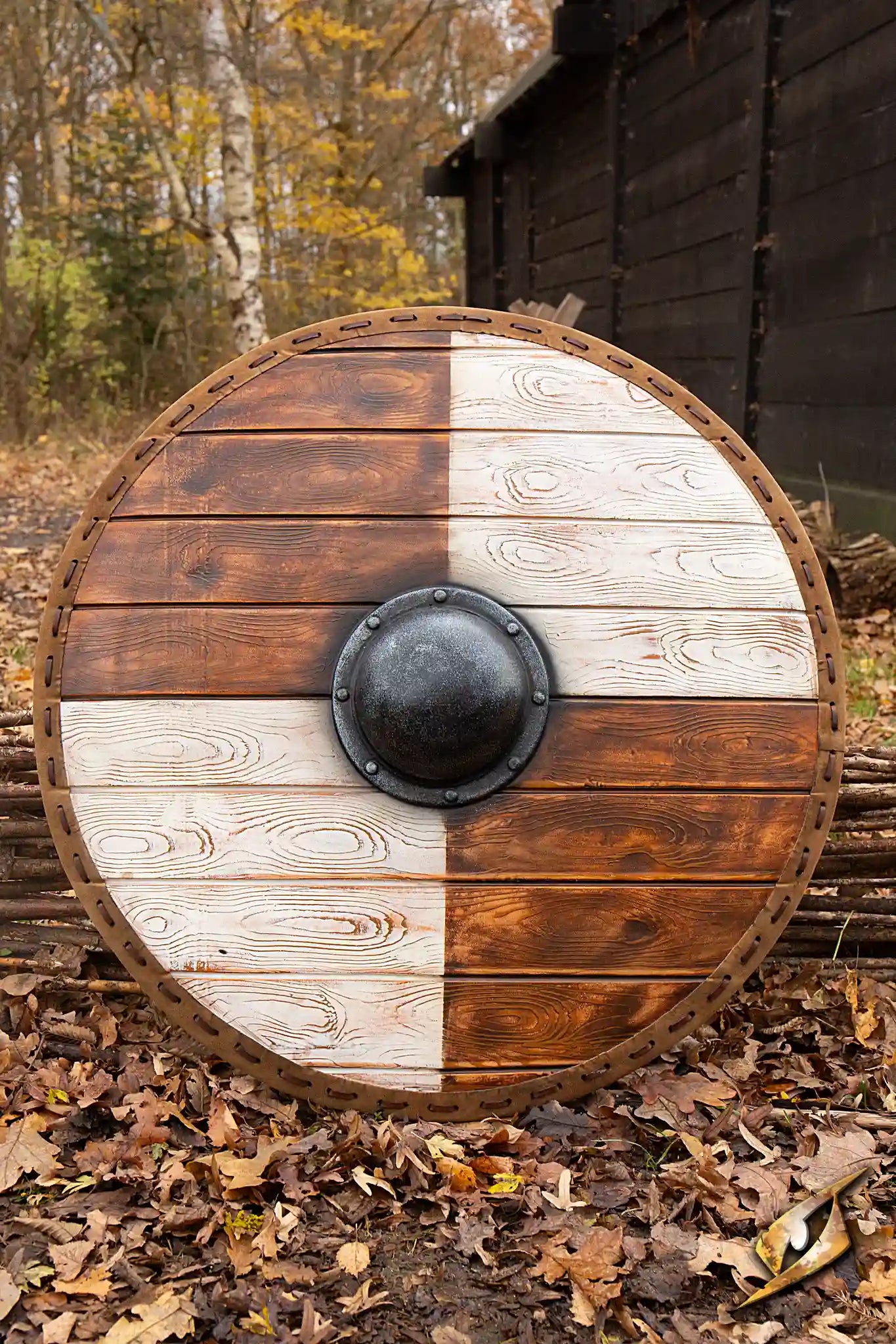 Viking Shields: wooden Viking shield with a metallic center, resting on leaves in a forest setting.