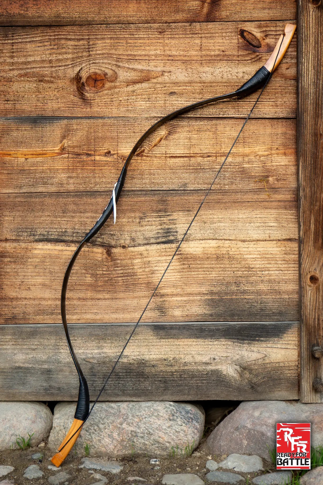 A traditional wooden bow hanging against a rustic wooden wall, part of the Bows collection at Epic Armoury.