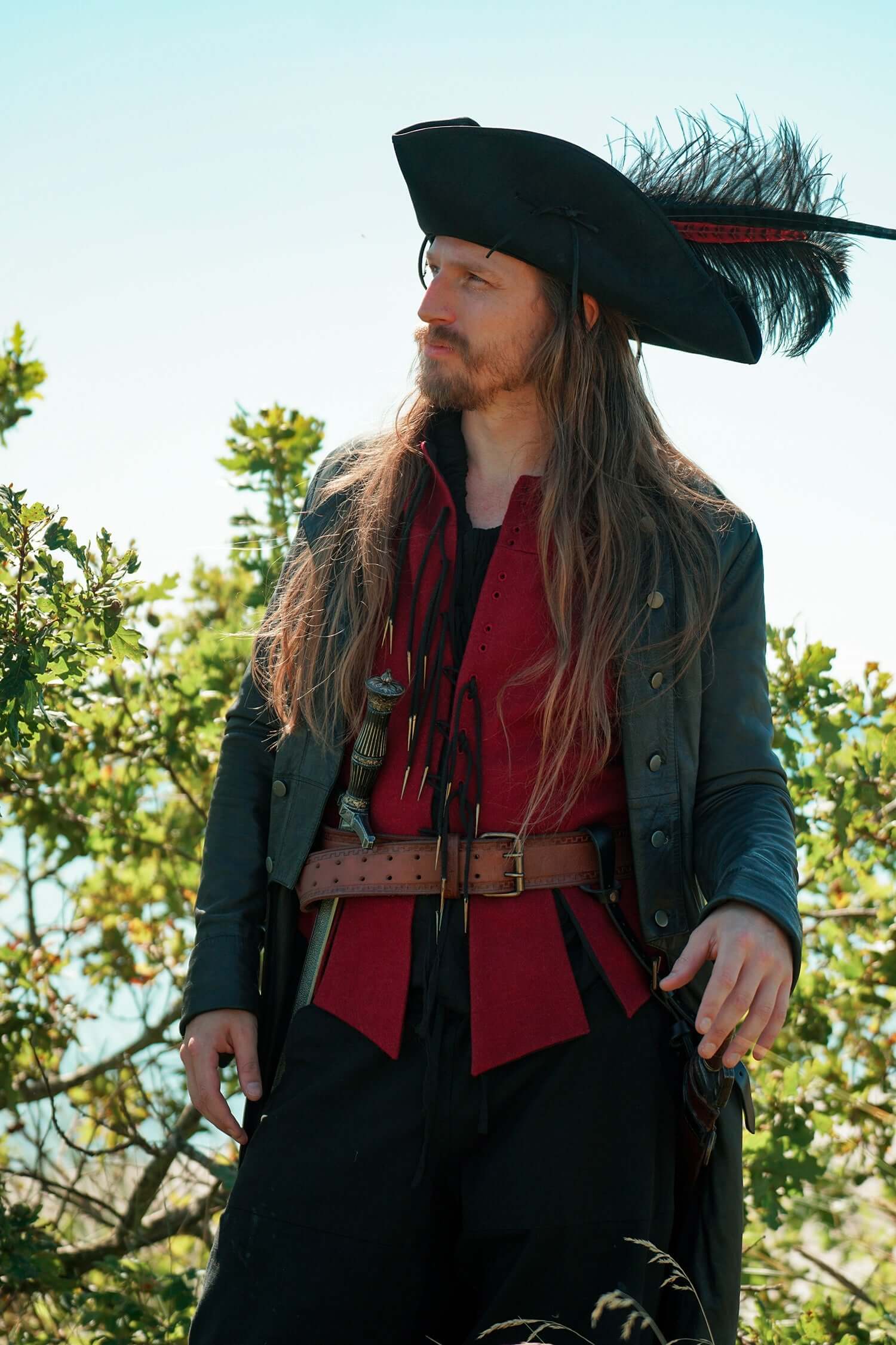 Renaissance Festival Gear featuring a man in a feathered hat and pirate attire surrounded by greenery.