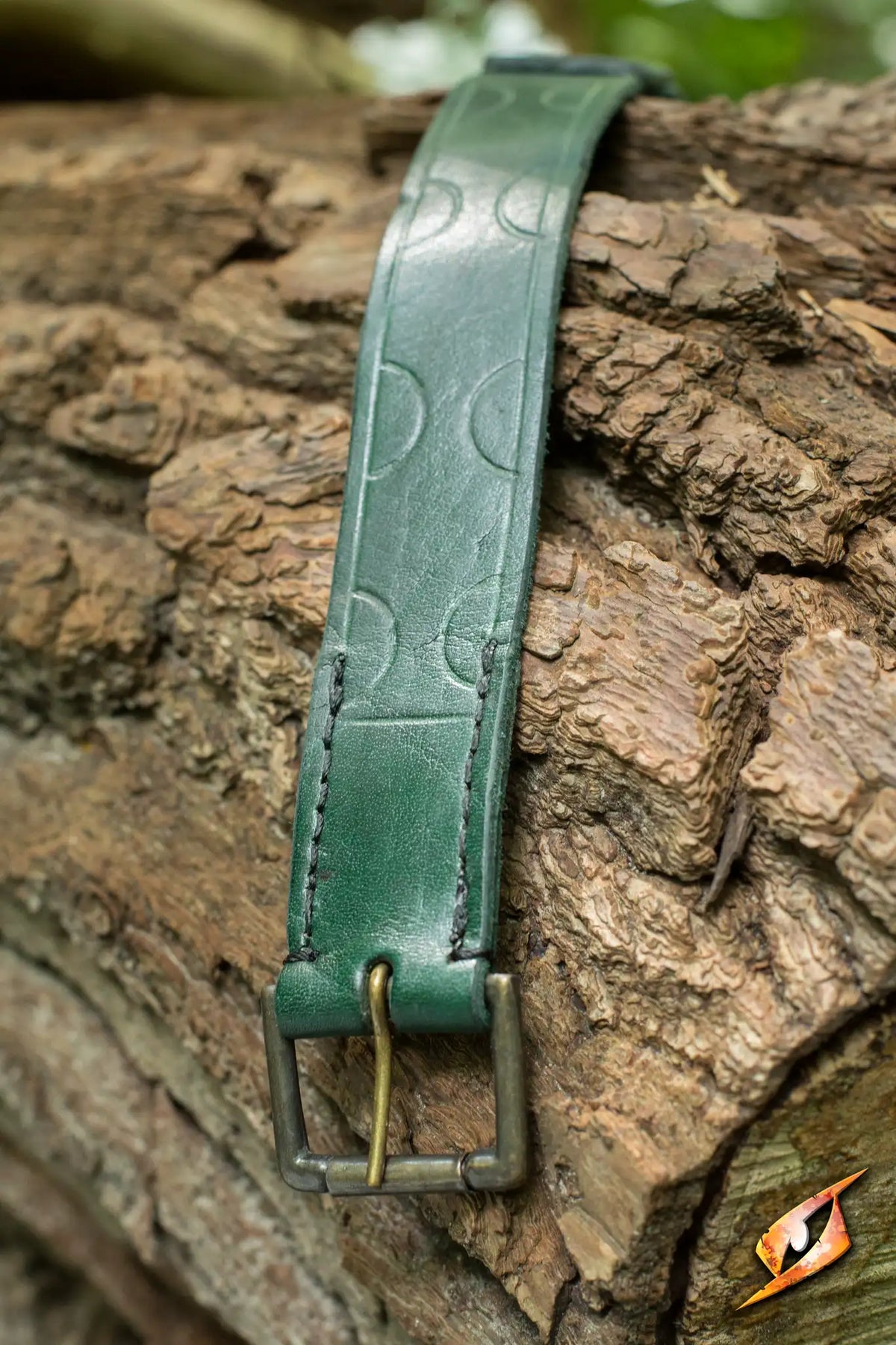 Aruthian Belt displayed on a rustic log, featuring a green leather strap with decorative stitching and buckle.
