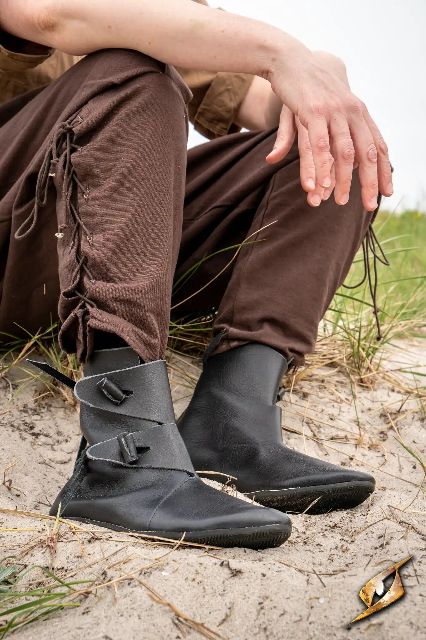 Shoes Jorik worn by a person sitting on the ground, featuring a black leather design and unique lacing.
