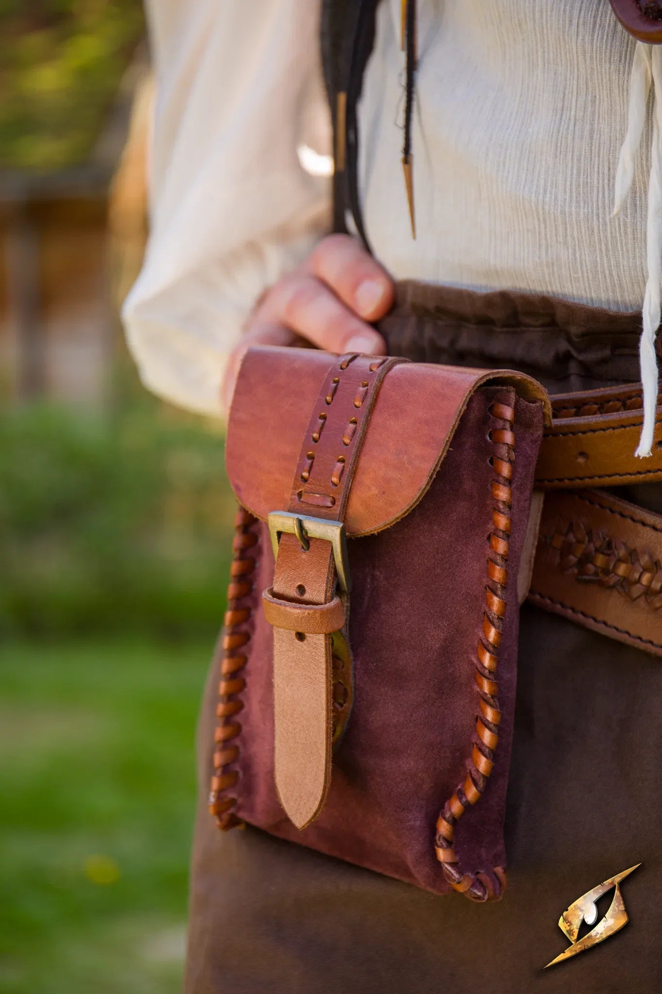 Merchant Suede Bag displayed on a person's side, featuring intricate stitching and a buckle closure.