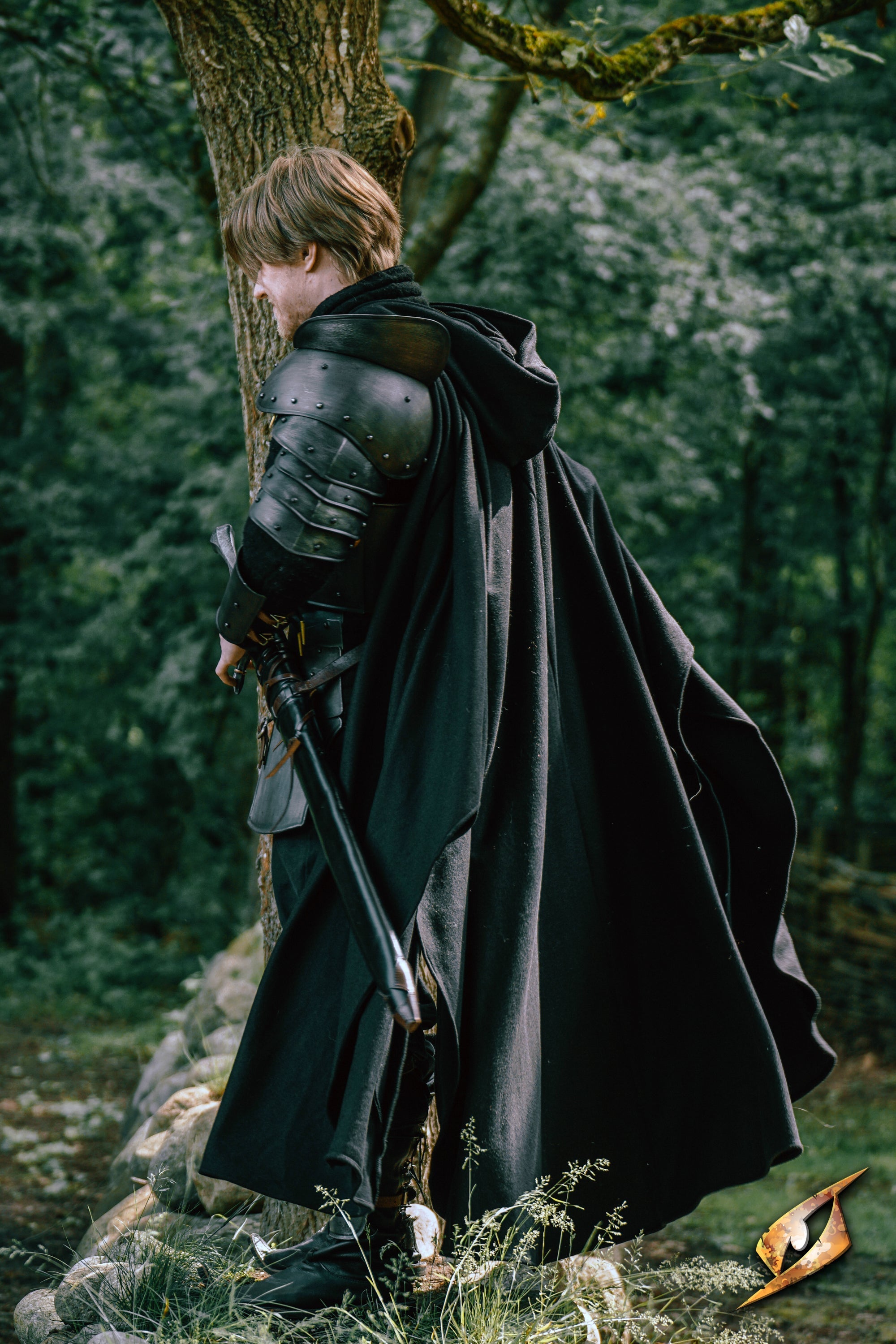 A child wearing a hooded Cape Godfrey Wool standing with a sword, set in a forested area.