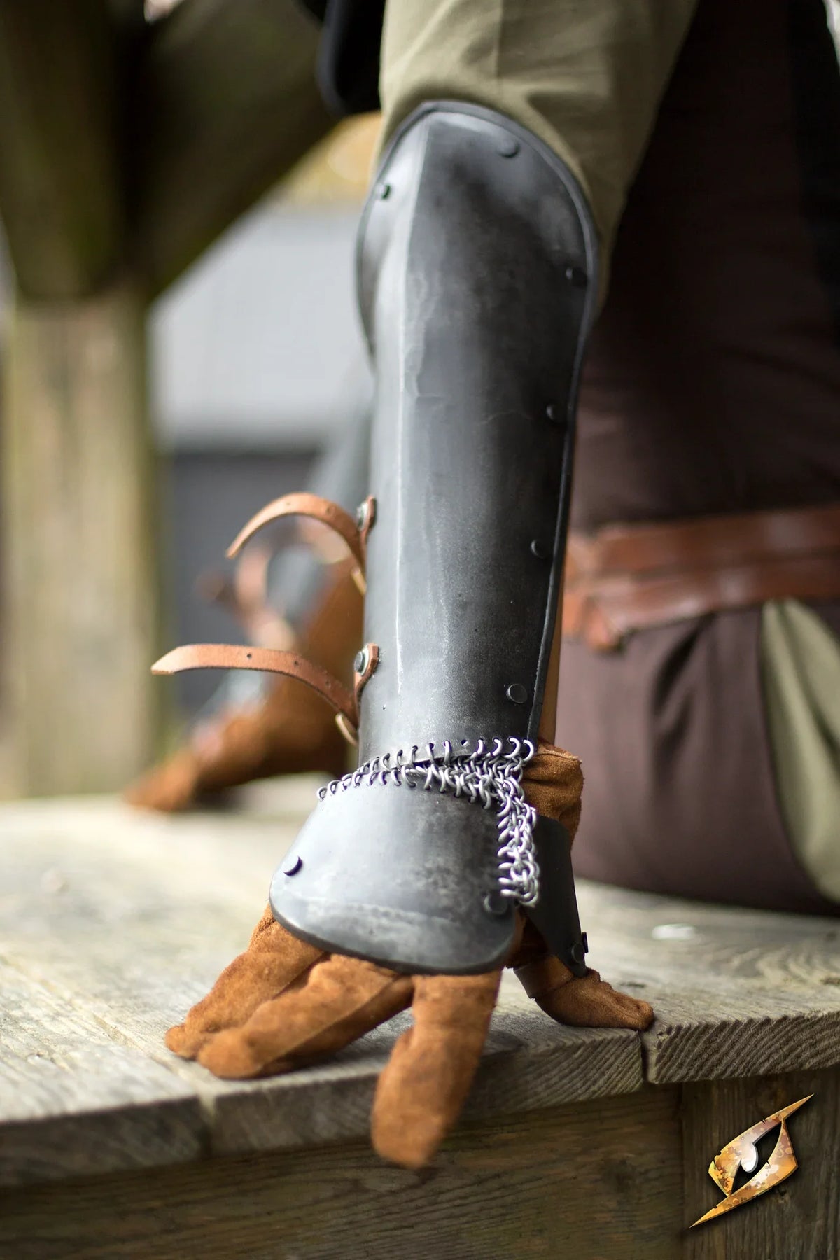 Close-up of a polished steel Bazuband on an arm, showcasing its design and integration with leather gloves.