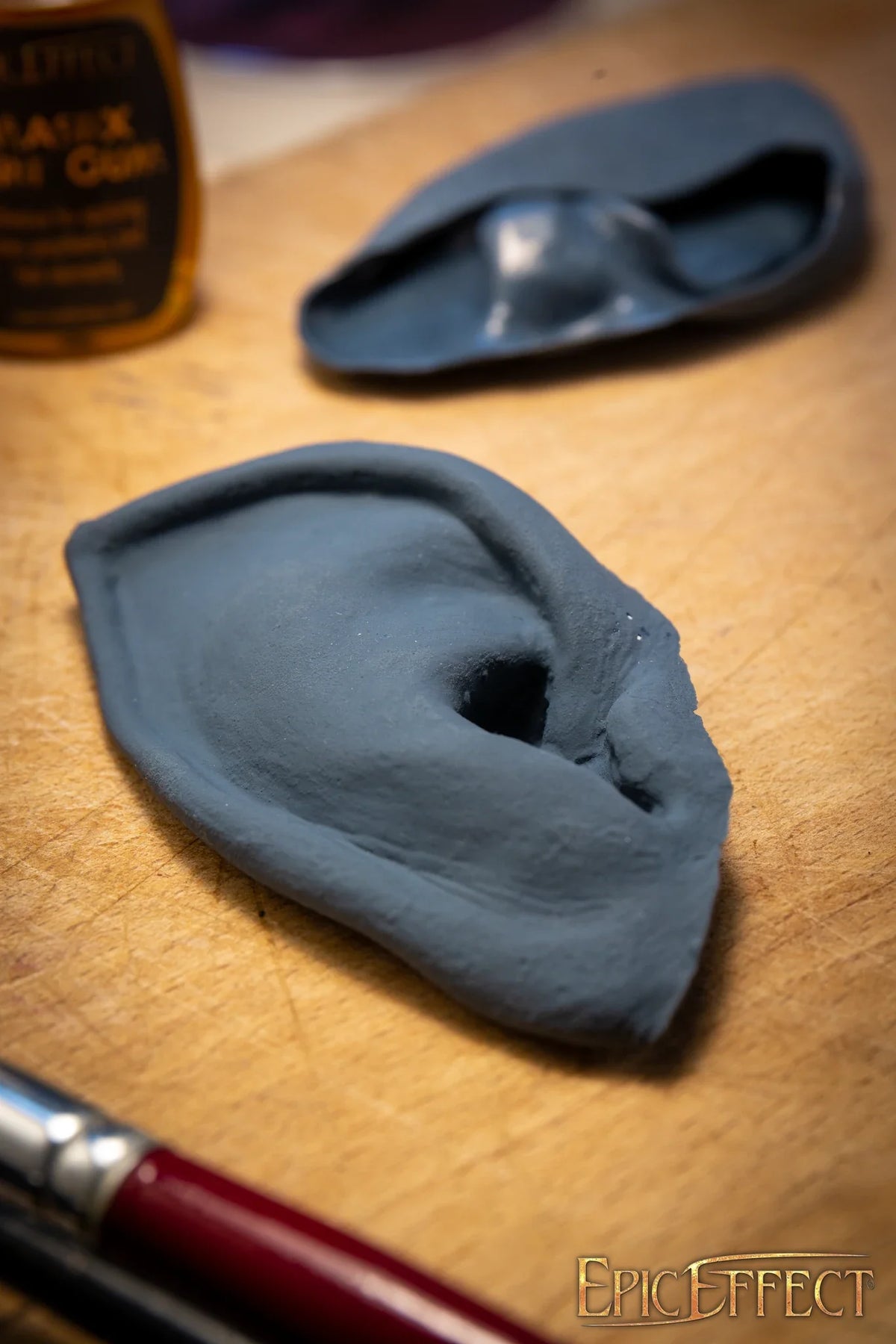 Halfling Ears sculpted from gray material on a wooden surface with a paintbrush nearby.