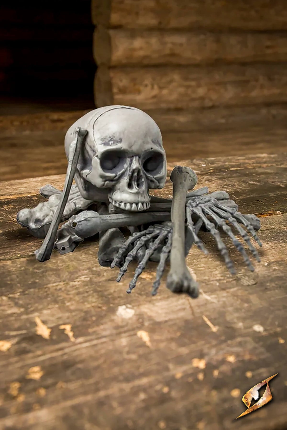 A realistic gray plastic skeleton decoration arranged with a skull, crossed bones, and skeletal hands on a rustic wooden surface.