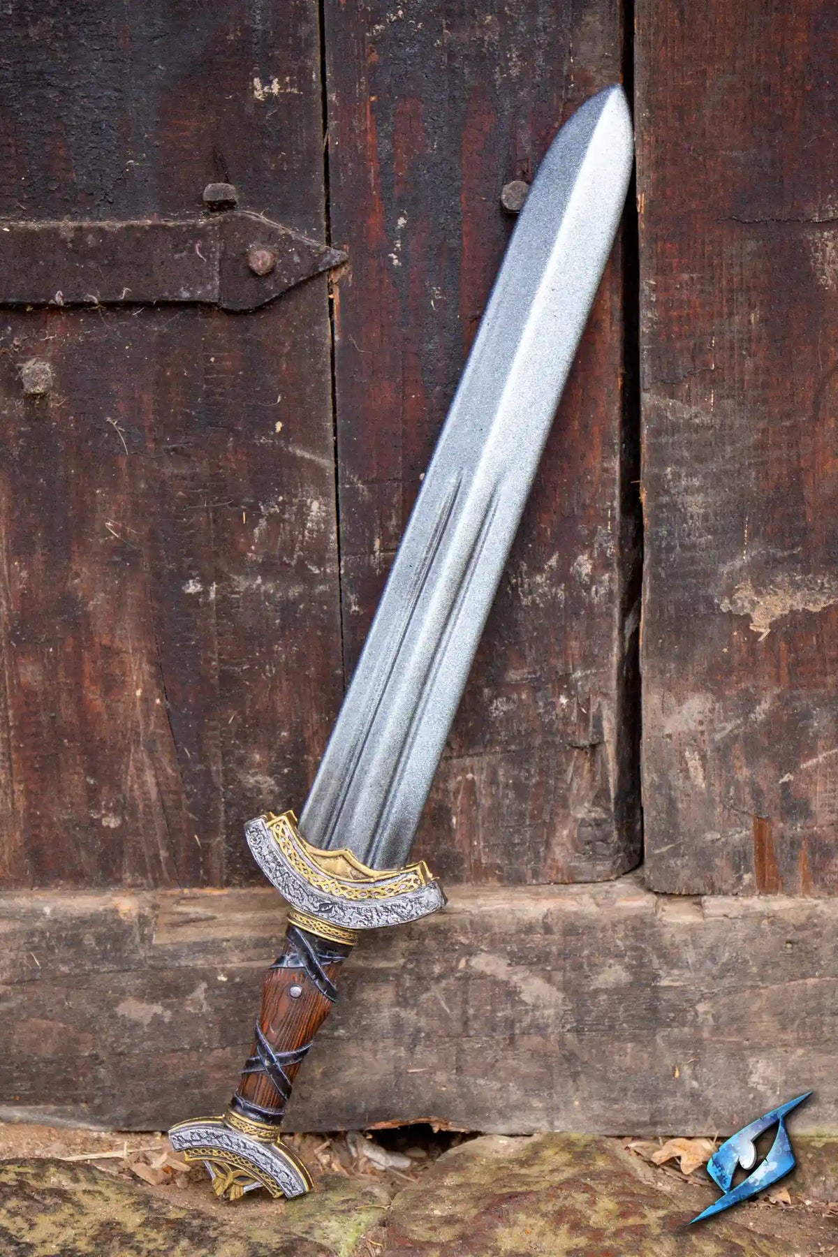 Warlord Sword resting against a wooden door, showcasing its ornate handle and double fuller blade design.