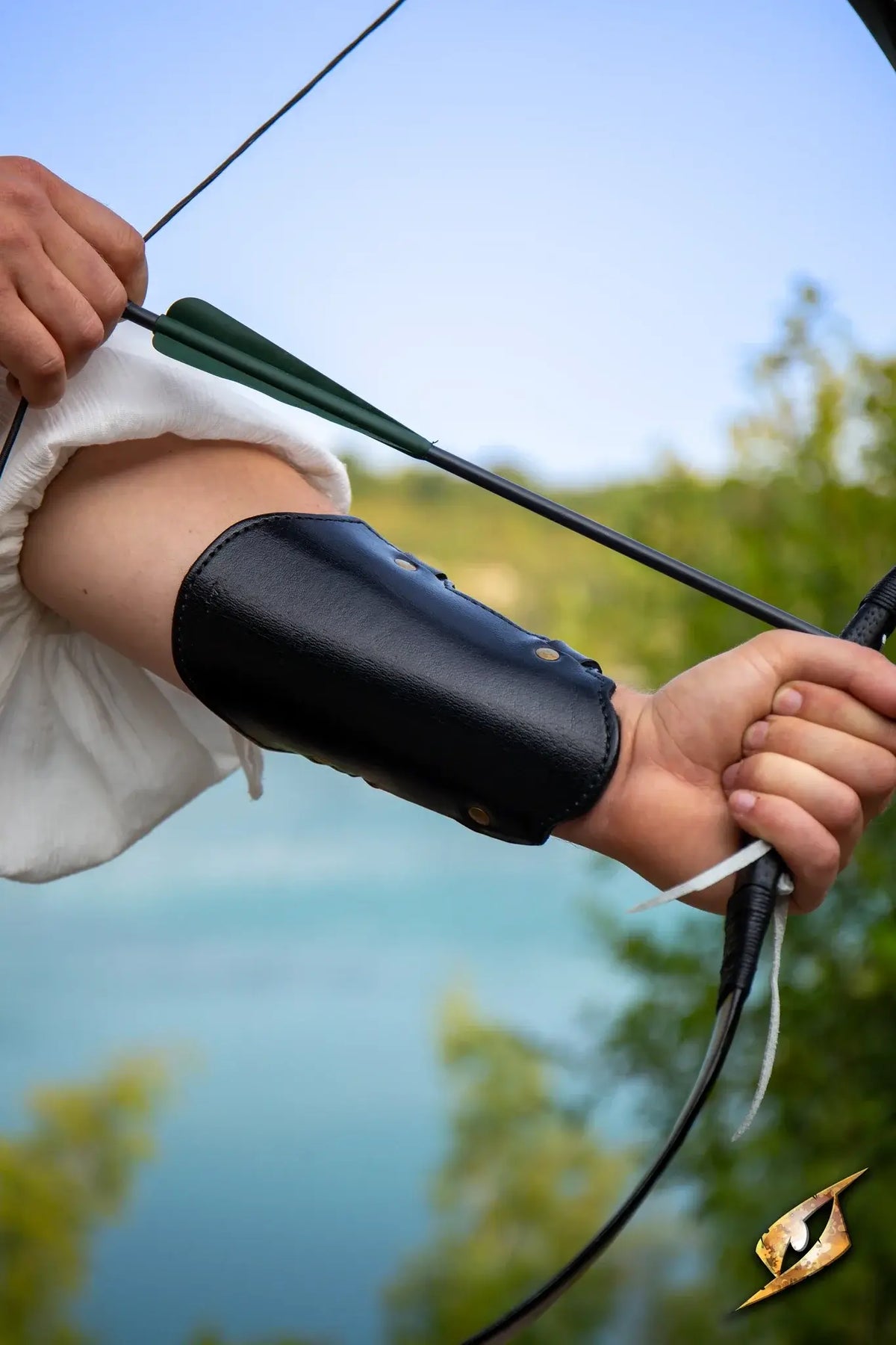A person wearing an Archery Bracer while aiming their bow by a scenic lake.