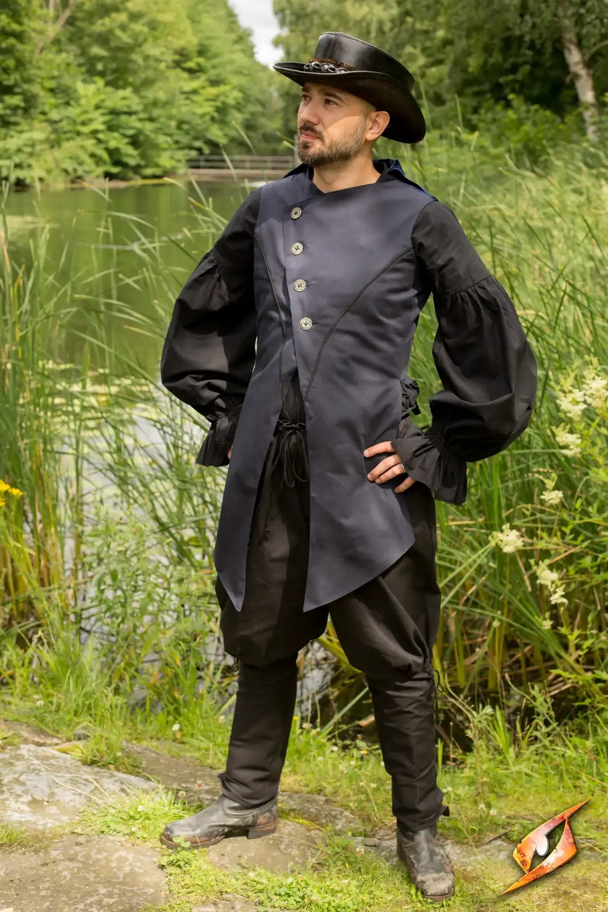 Man wearing an Epic Black Vest Dorian standing by a serene lake surrounded by lush greenery.