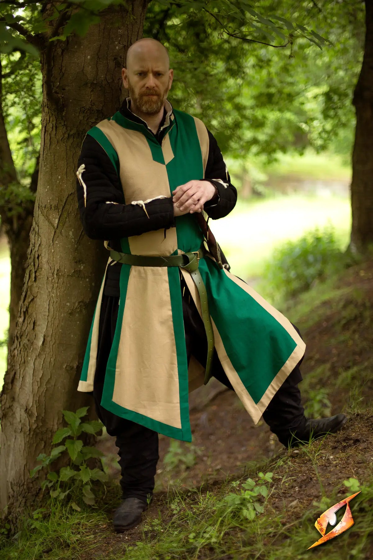 A man in a green and beige Basic Tabard stands by a tree, ready for a rescue mission.