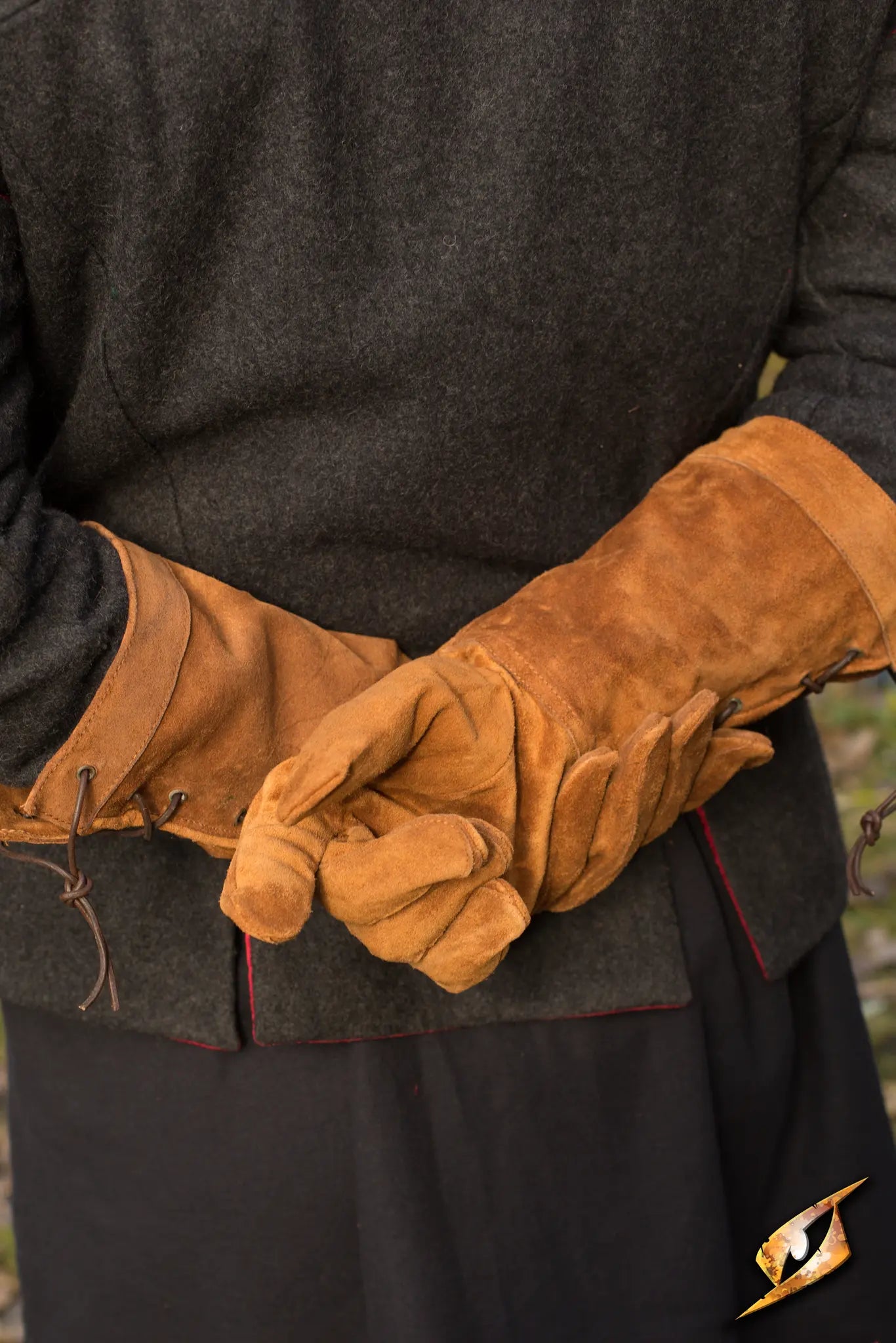 A pair of tan leather gloves worn by a person with arms crossed.
