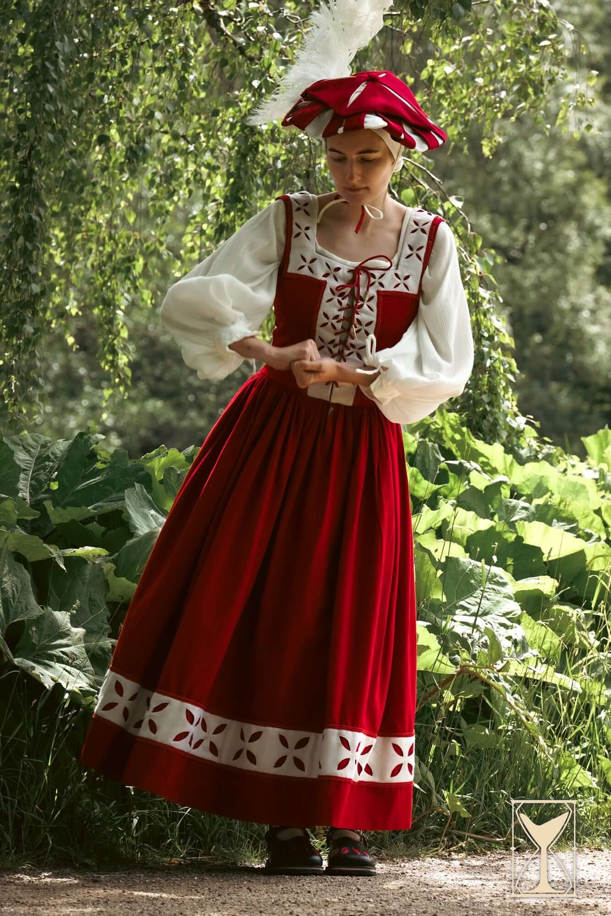 Woman wearing a Kampfrau dress in rich red and white, showcasing historical Landsknecht style in a natural setting.