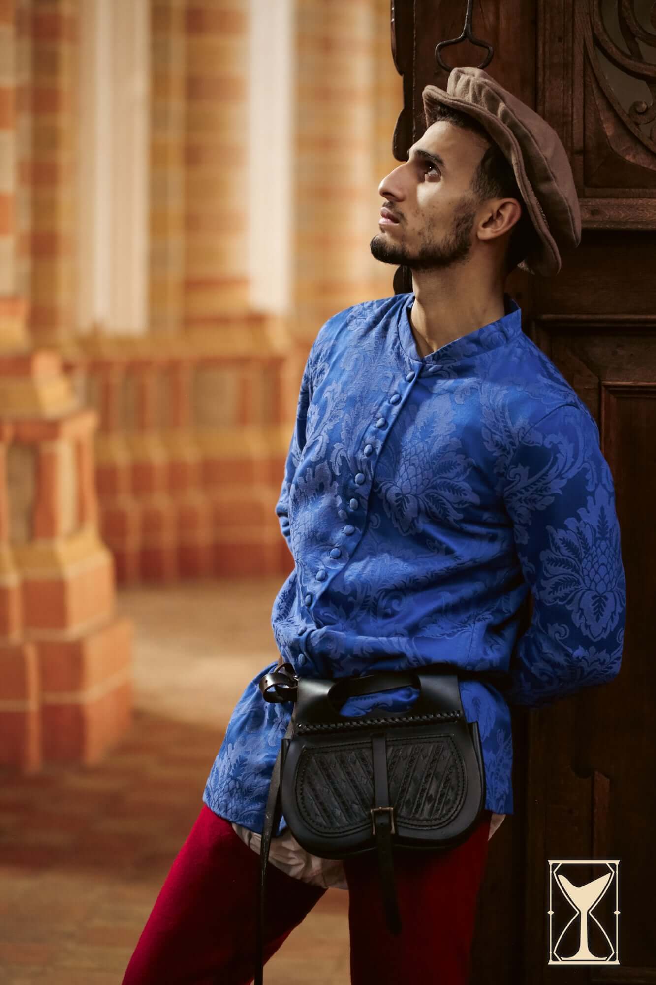 Cotehardie Rodrigo blue brocade button-up jacket with jacquard pattern, worn by model in historic setting.