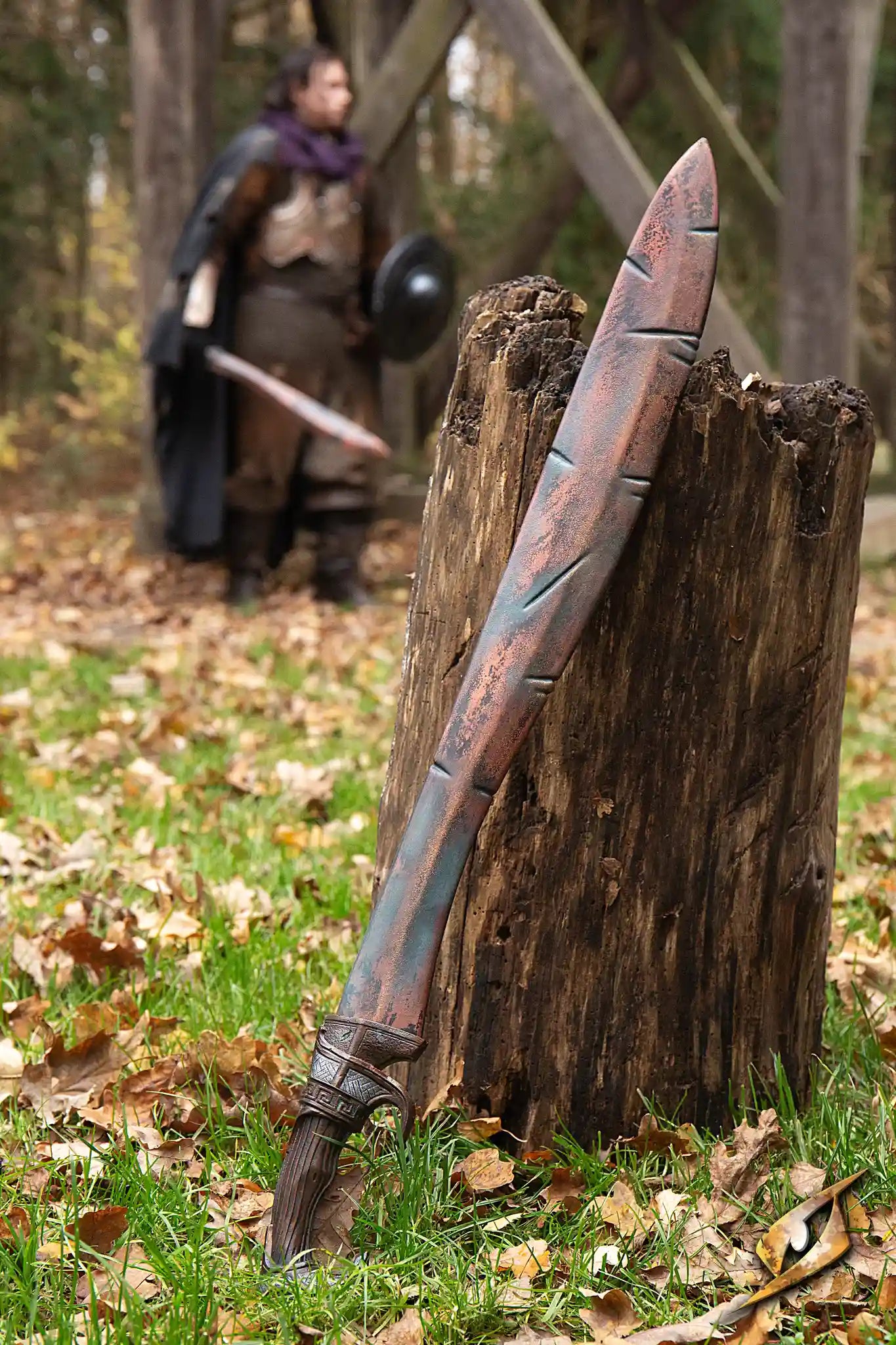 Battleworn Falcata resting on a tree stump, showcasing its unique design amidst an outdoor setting.