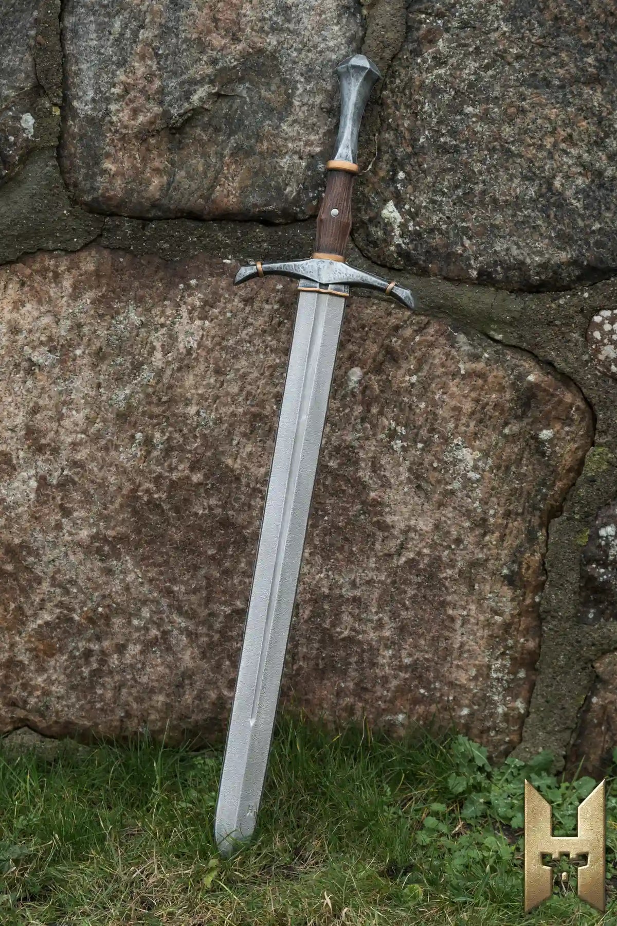 Bastard Sword leaning against a rocky wall, showcasing its detailed hilt and fullered blade.