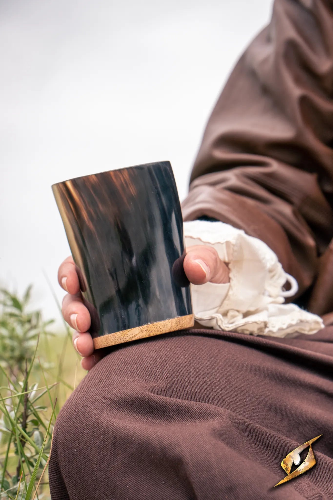 Adventurer Horn Cup held by a person in period clothing, featuring a dark horn finish and wooden base.