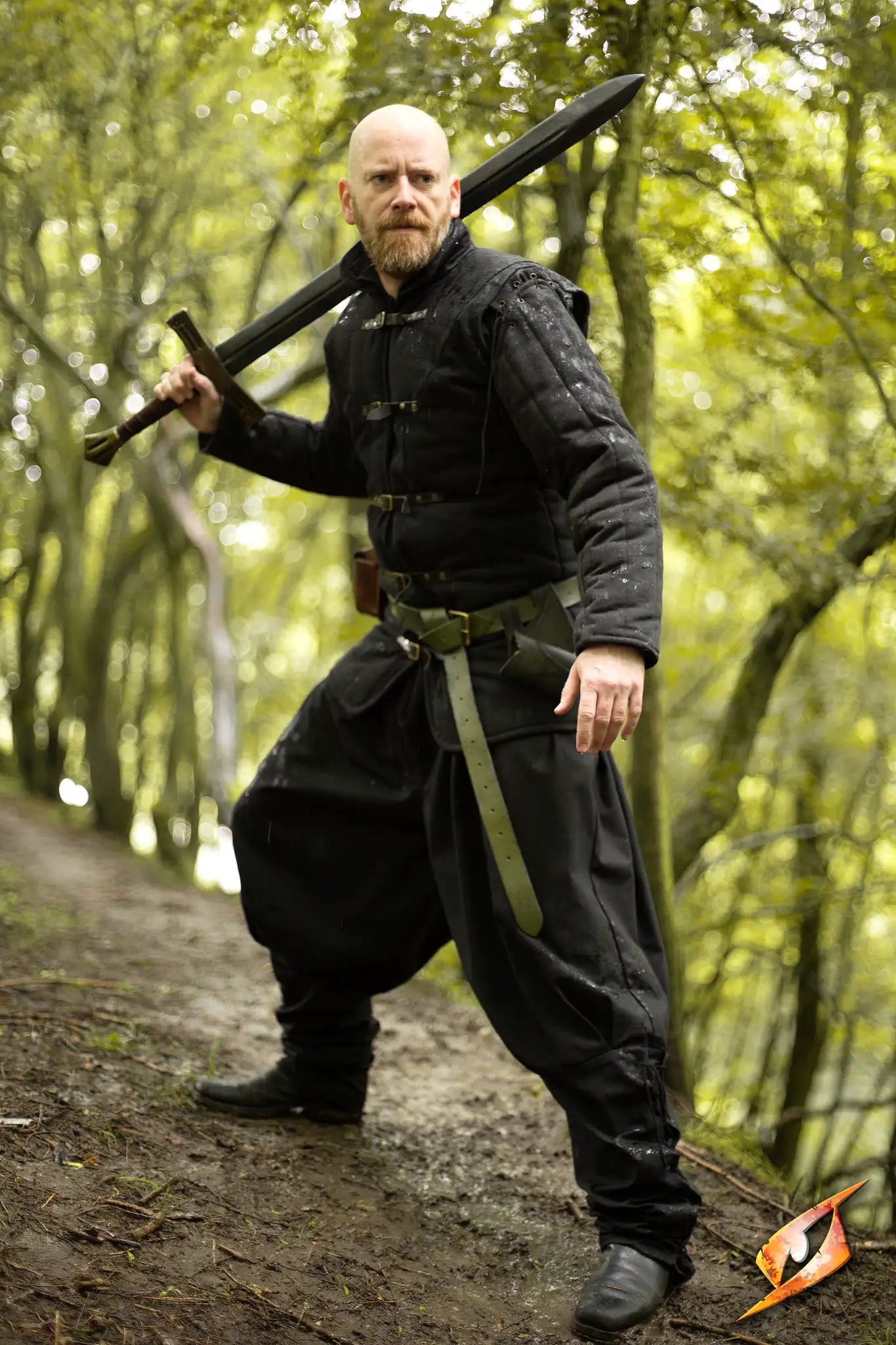 Gambeson Warrior With Long Sleeves standing in a forest, holding a sword confidently.