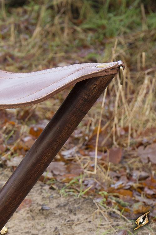 Close-up of a Tripod Stool leg, showcasing the durable wood and leather construction in a natural outdoor setting.