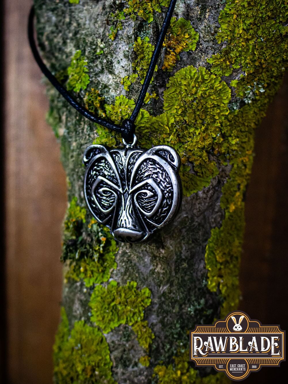 Bear Clan Pendant showcasing a detailed bear's head design, symbolizing strength, hanging from a black cord on a tree.